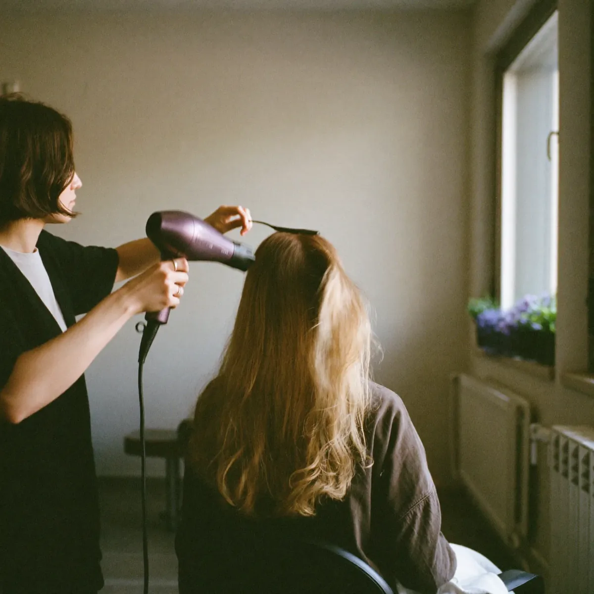 A stylist blow-drying a client's hair at the styling chair