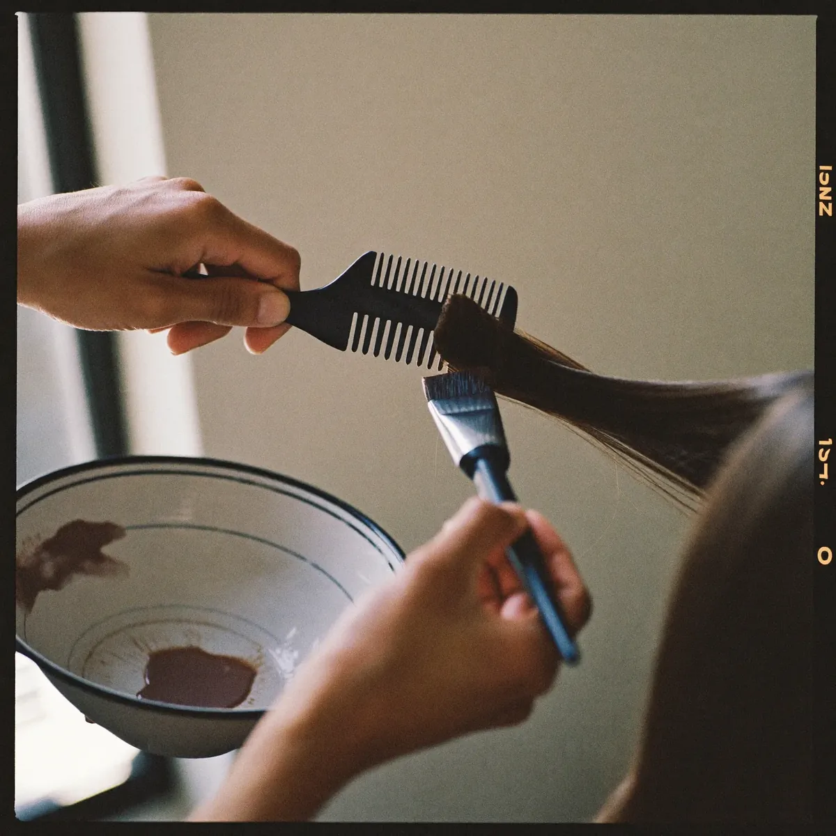 Hands sectioning hair and applying colour with a tint brush